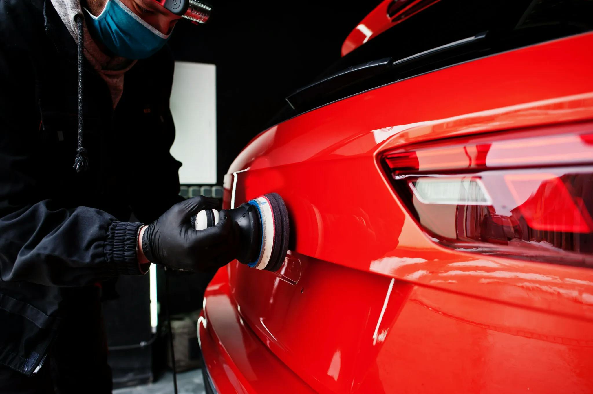 une personne portant un masque et des gants polissant une voiture rouge